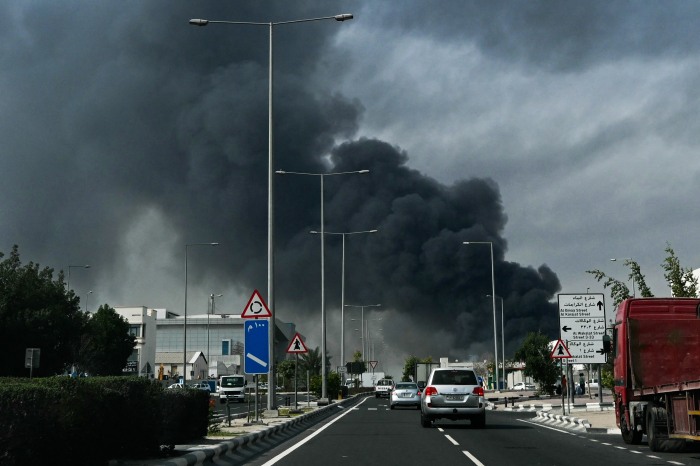 سقوط آرامش دبی؛ چگونه جنگ ایران تصویر لوکس خلیج فارس را بر هم زد؟ Vehicles driving on a street with a large plume of dark smoke rising in the background.