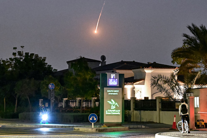 سقوط آرامش دبی؛ چگونه جنگ ایران تصویر لوکس خلیج فارس را بر هم زد؟ A cyclist watches a bright projectile falling through the dark sky over Dubai.