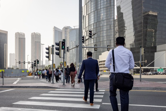 سقوط آرامش دبی؛ چگونه جنگ ایران تصویر لوکس خلیج فارس را بر هم زد؟ People crossing a street at a crosswalk in Dubai's Business Bay financial district, with modern skyscrapers in the background.